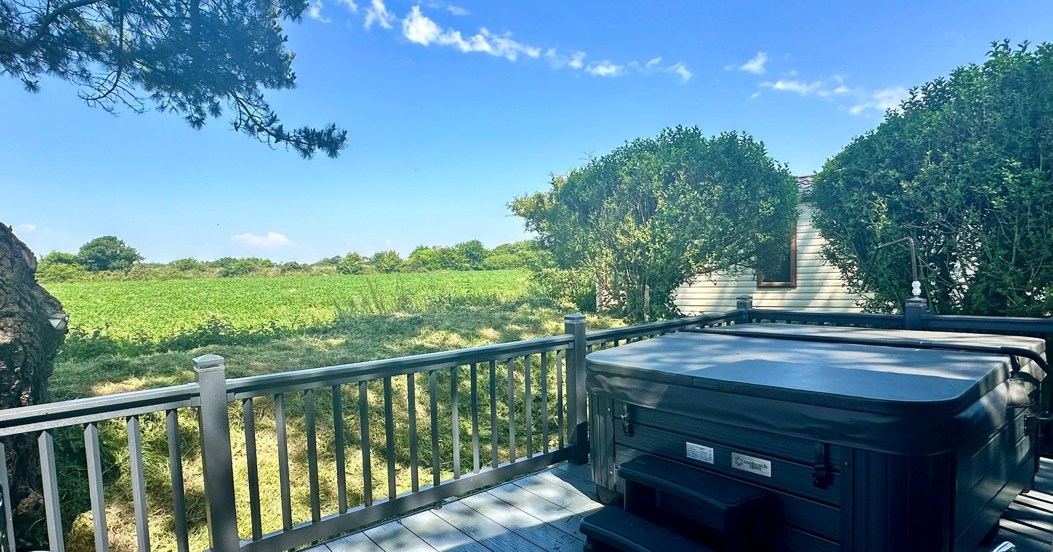 Hot tub on a wooden deck overlooking green fields under a blue sky