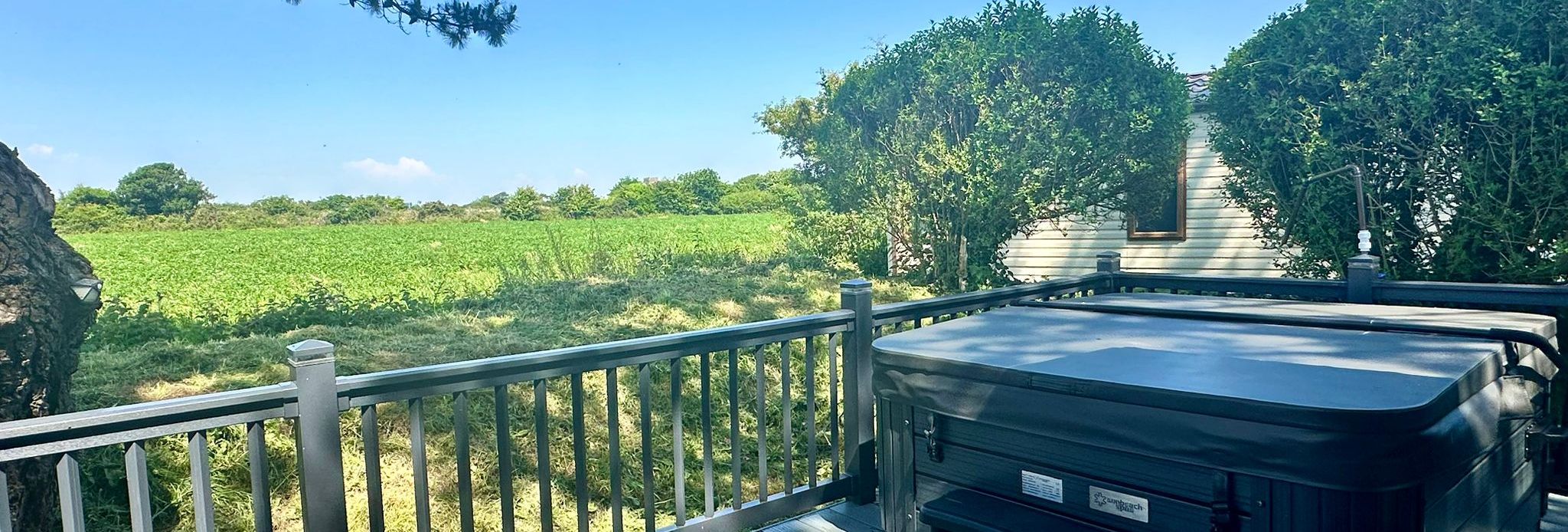 Hot tub on a wooden deck overlooking green fields under a blue sky