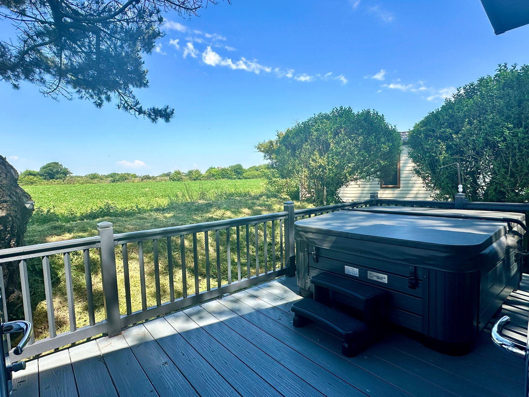 Hot tub on a wooden deck overlooking green fields under a blue sky