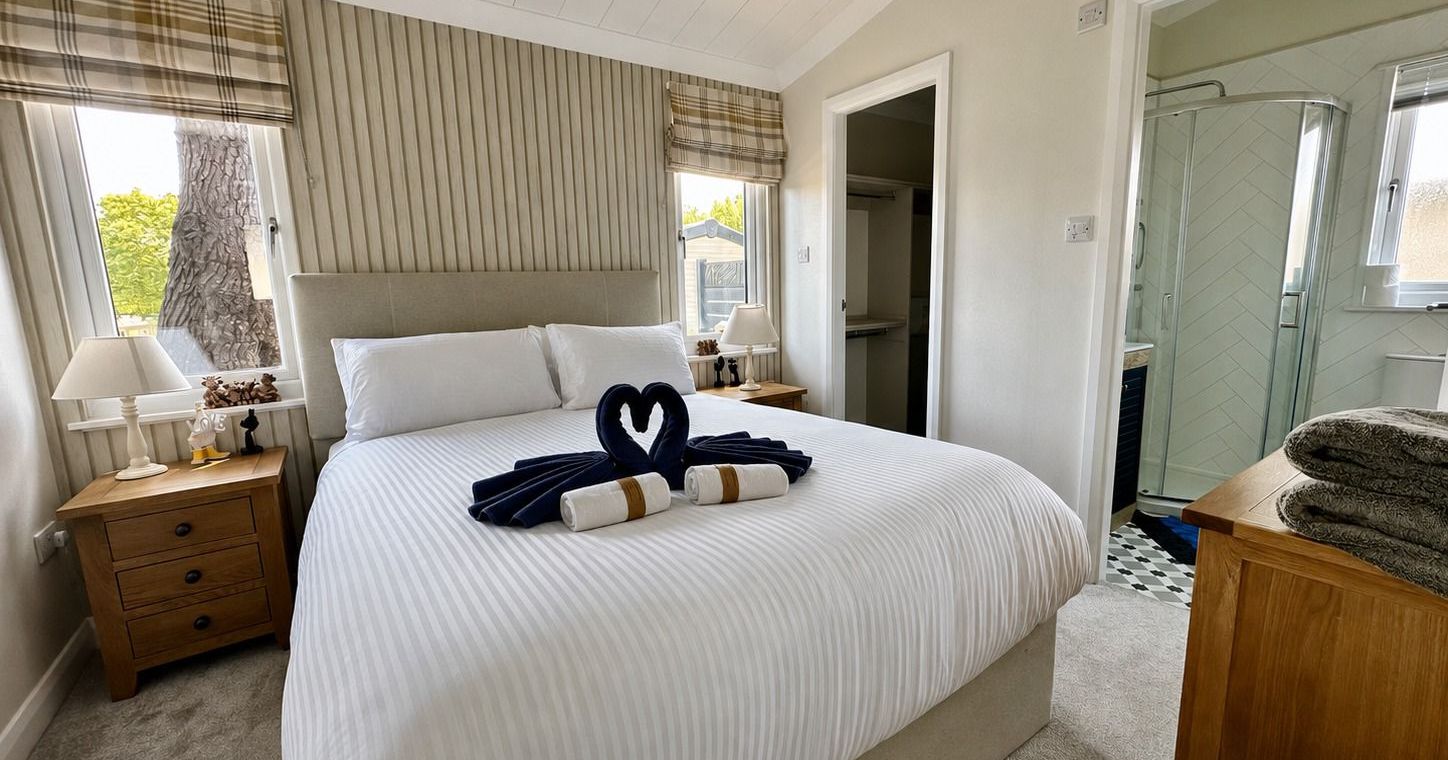 Bright double bedroom with white bedding, wooden bedside tables, and an en-suite shower room
