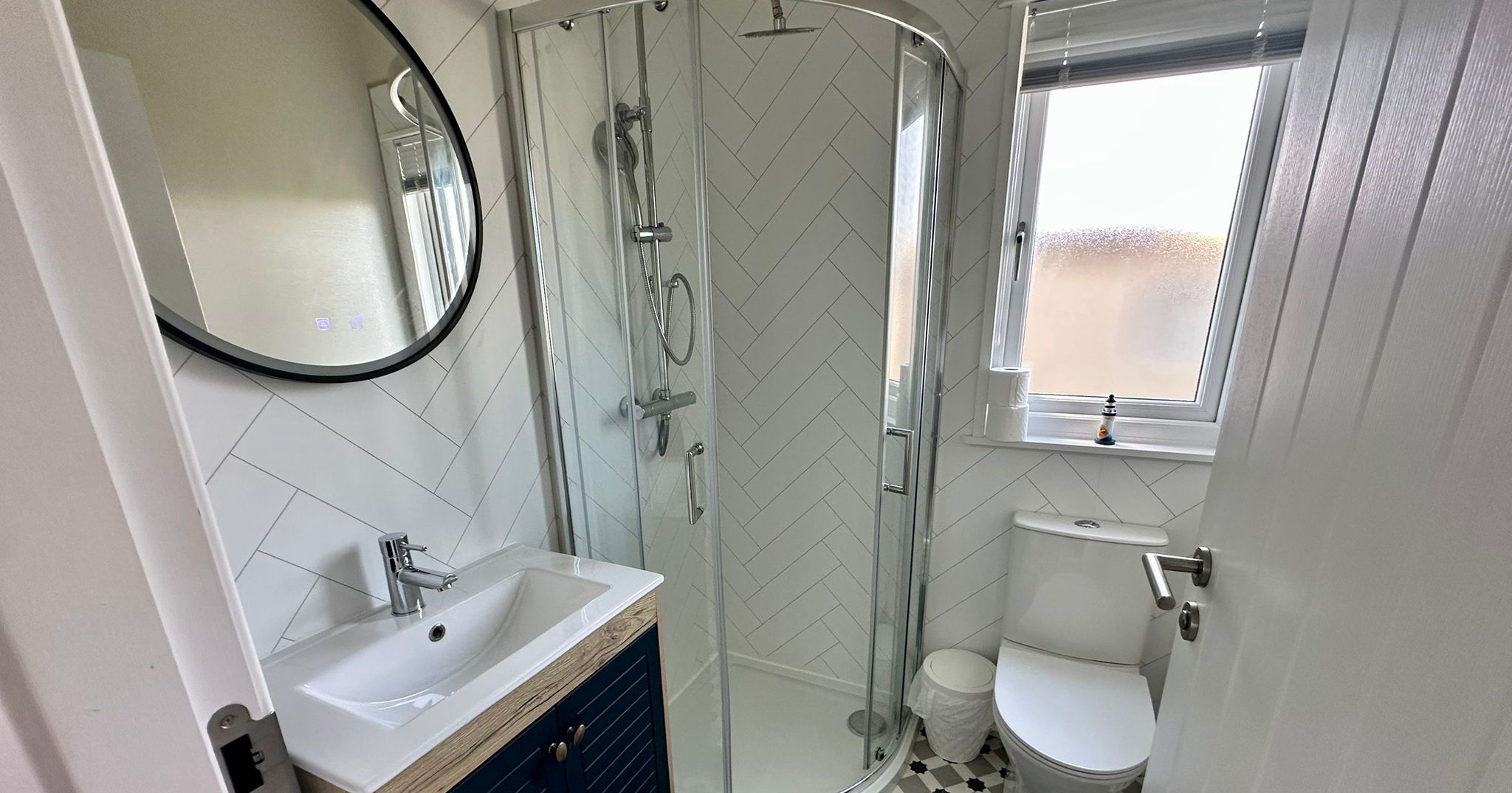 Compact modern bathroom with corner shower, white herringbone wall tiles, vanity unit and toilet