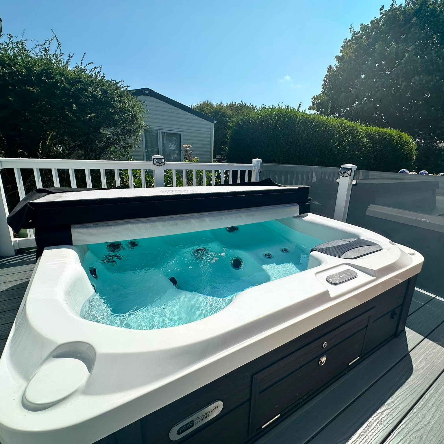 Outdoor hot tub on a decking area beside a caravan, with bubbling water and a clear blue sky
