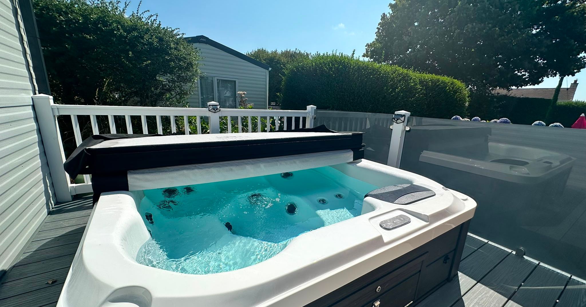 Outdoor hot tub on a decking area beside a caravan, with bubbling water and a clear blue sky