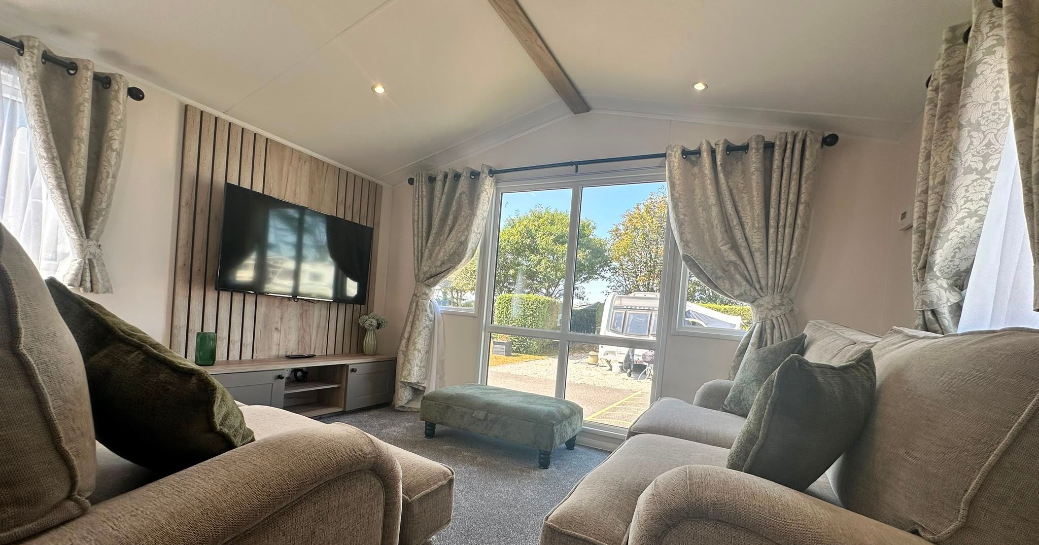 Cosy lounge with two beige sofas, wall-mounted TV and large window with patterned curtains