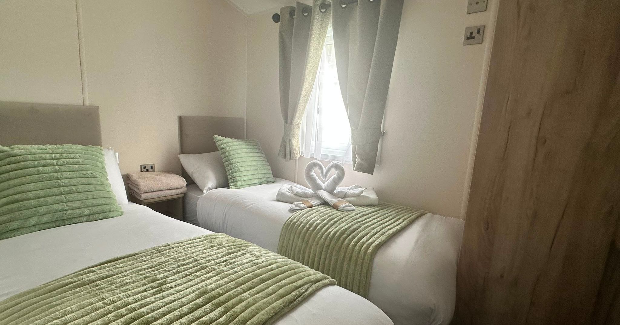 Twin bedroom with green bed runners, grey curtains and towel swans on one bed
