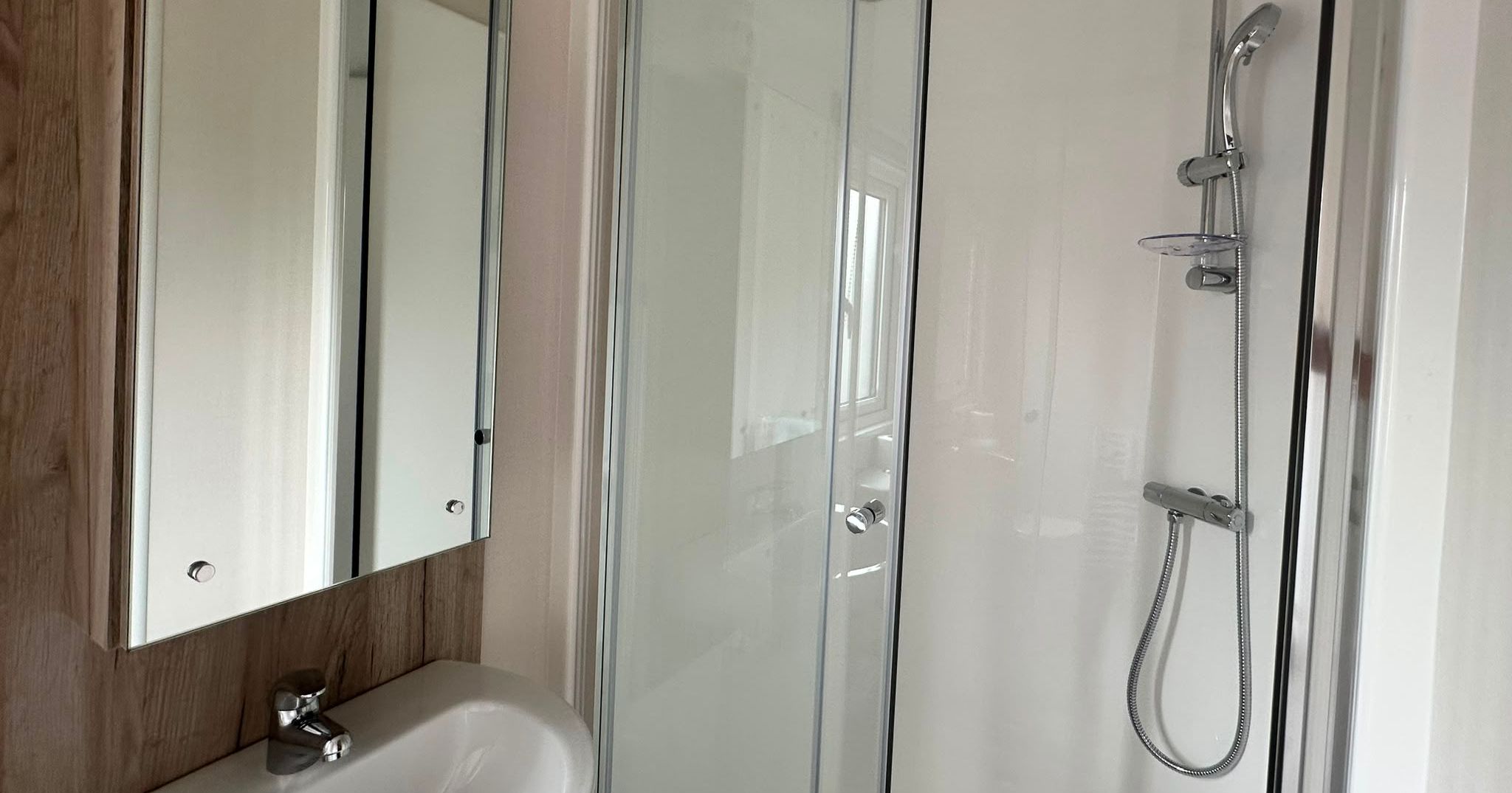 Modern bathroom with glass shower enclosure, chrome shower fittings, wall mirror and white basin