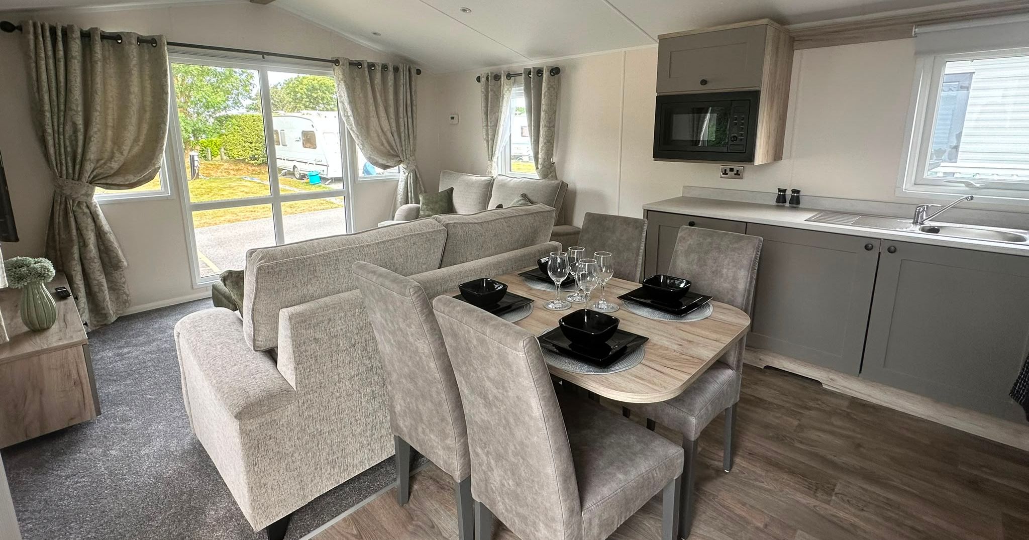 Open-plan static caravan living and dining area with grey sofa, four-seat table set and compact kitchen