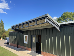 Metal building with green corrugated walls, brick base, and a flat overhanging awning above a doorway.