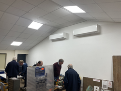 Group of older men examining items on tables in a room with white walls and air conditioning units