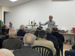 A man giving a technical demonstration to an audience in a classroom or workshop setting.