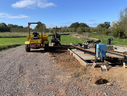 Construction site with yellow dumper, excavator, and railway track under construction in a rural area