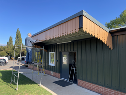 Person standing on scaffolding working on the decorative trim of a green metal building with a brick base.