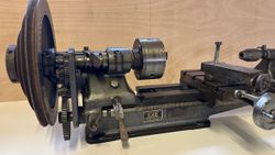 Close-up view of a vintage metal lathe with gears and labeled plaques.