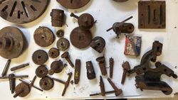 Assorted rusty metal lathe parts and gears laid out on a white surface.