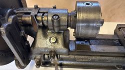 Close-up view of a vintage metal lathe chuck and carriage assembly.