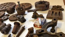 Collection of rusty metal machine parts and gears on a white surface.