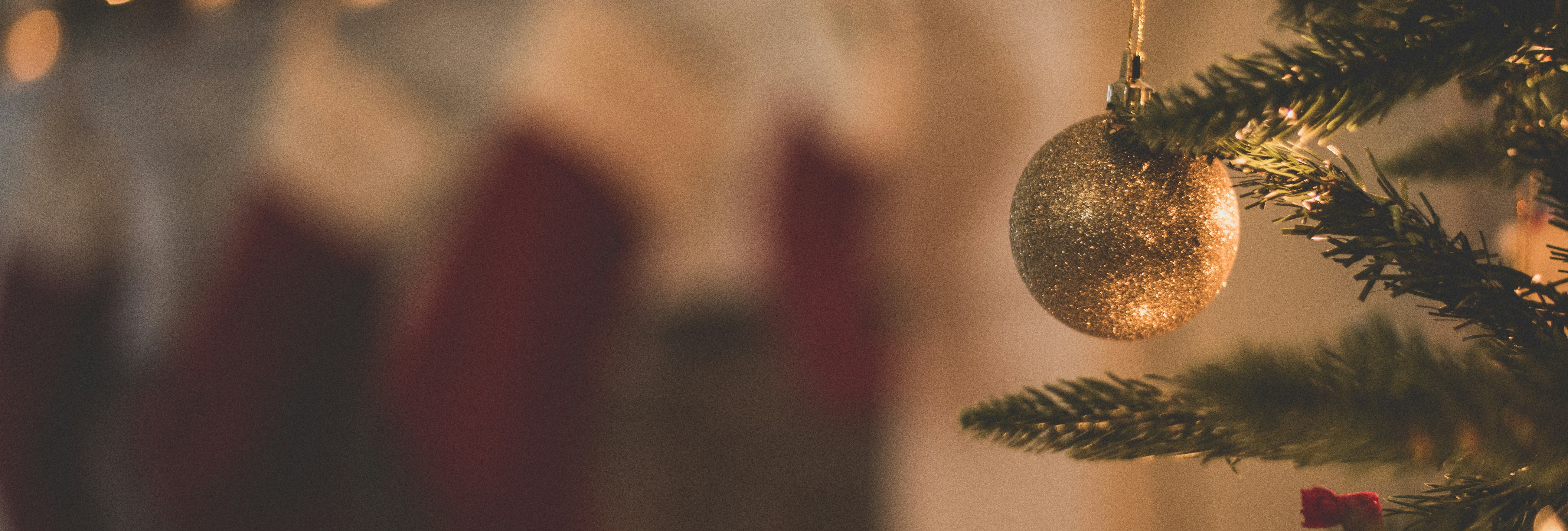 Close-up of a Christmas tree ornament with stockings and holiday lights in the background