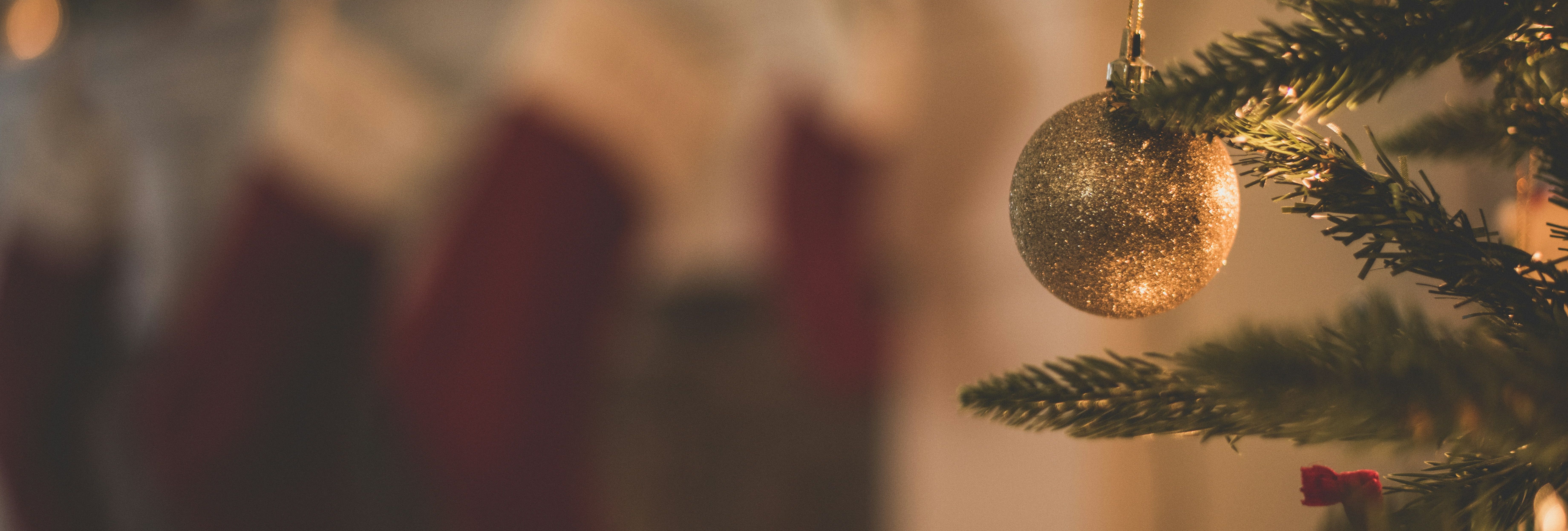 Close-up of a Christmas tree ornament with stockings and holiday lights in the background