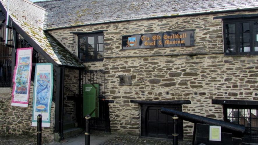 Exterior of The Old Guildhall Gaol & Museum, a historic stone building with banners and a cannon outside.