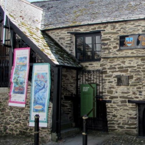 Exterior of The Old Guildhall Gaol & Museum, a historic stone building with banners and a cannon outside.