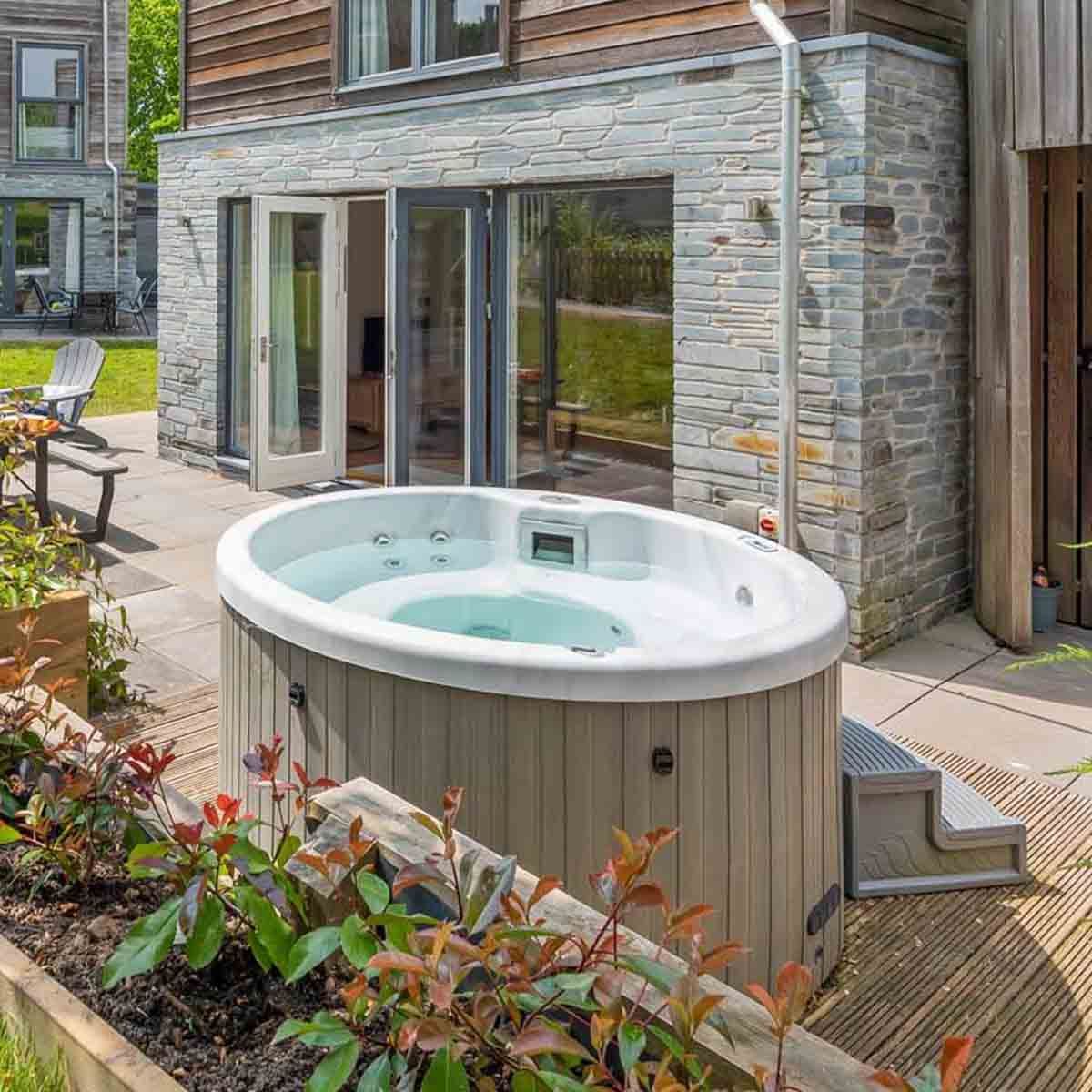 Outdoor hot tub next to a modern house with patio and open doors