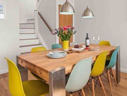 Modern dining room with multicolored chairs, a wooden table, flowers, wine, and staircase in the background