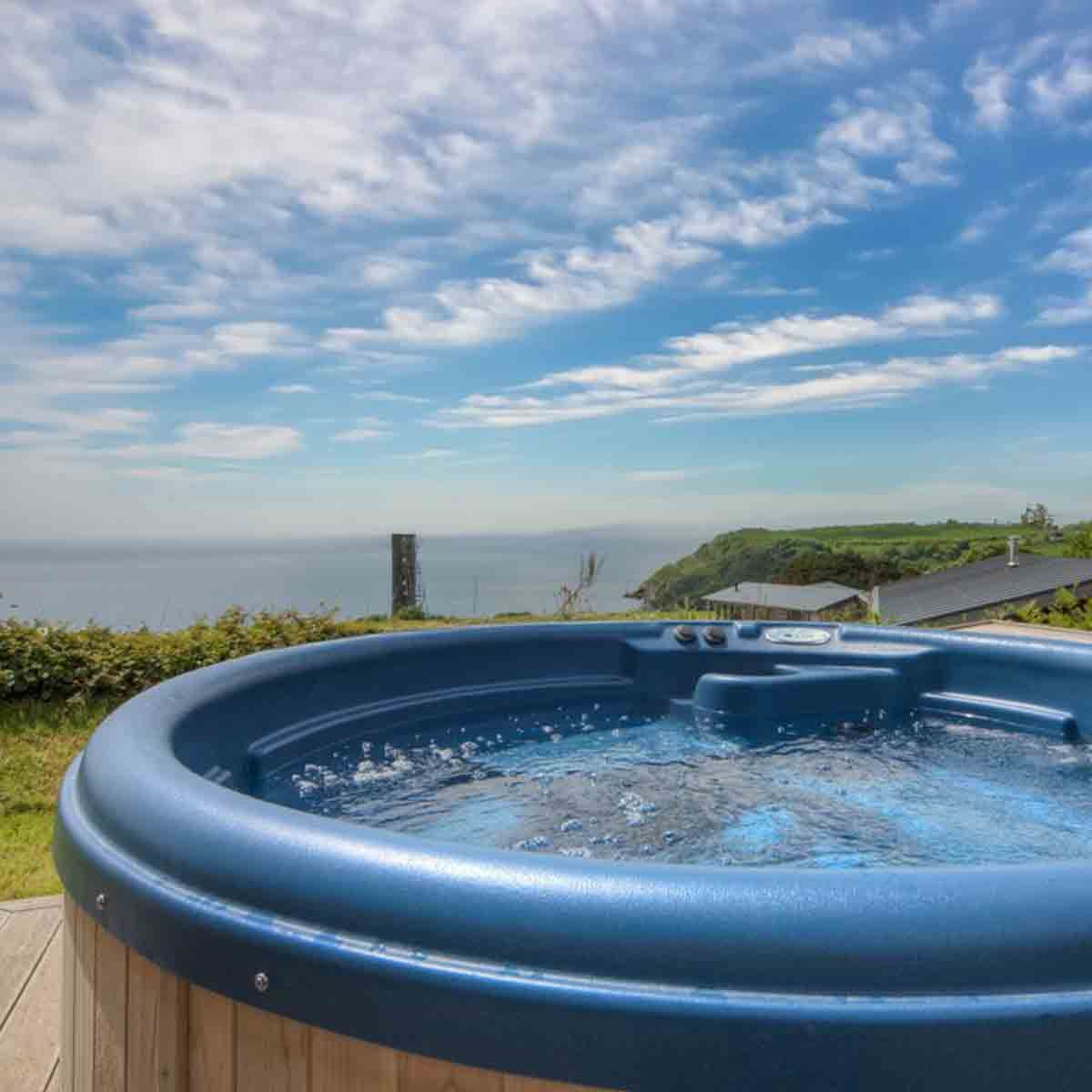 Outdoor hot tub overlooking the ocean and green hills under a blue sky with scattered clouds