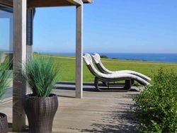 Outdoor deck with lounge chairs overlooking a grassy lawn and ocean