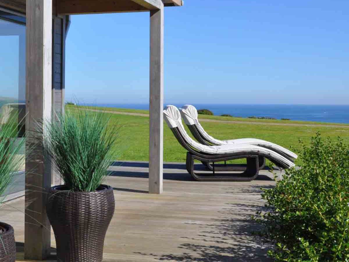 Outdoor deck with lounge chairs overlooking a grassy lawn and ocean