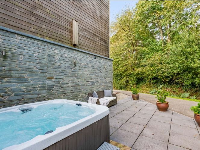 Outdoor patio area with hot tub, seating, potted plants, and surrounding greenery