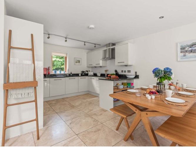 Modern kitchen and dining area with wooden table, bench seating, and white cabinets.