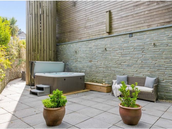 Outdoor patio area with hot tub, potted plants, and wicker seating