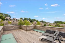 Modern rooftop terrace with wooden decking, lounge chairs, and views of contemporary houses surrounded by greenery.