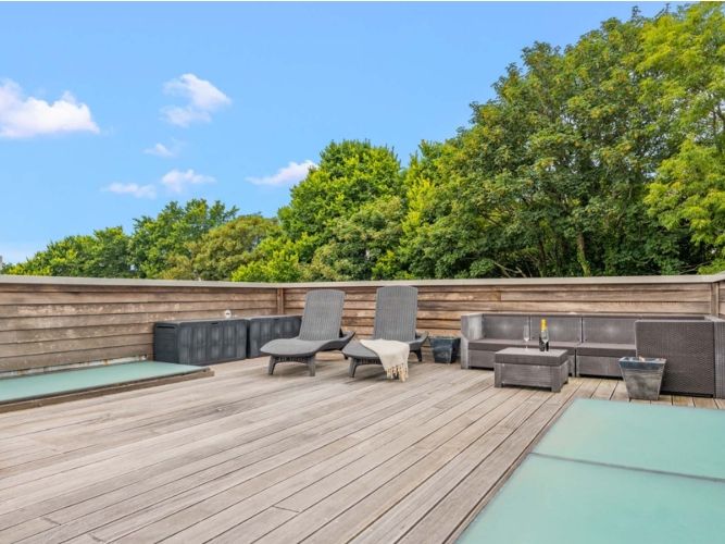 Spacious rooftop terrace with lounge chairs, outdoor sofa, and surrounded by wooden fencing and greenery.