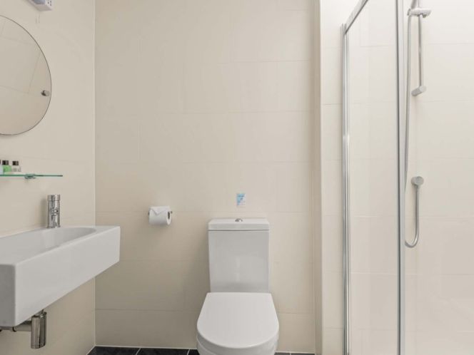 Modern white bathroom with toilet, sink, glass shower, and wall mirror