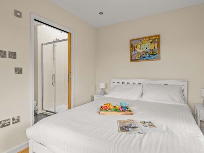 Cozy bedroom with white bedding, bedside tables, a tray with breakfast, and an ensuite bathroom.