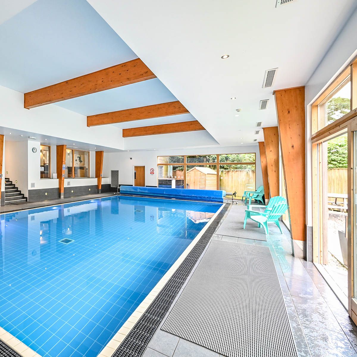 Indoor swimming pool area with wooden beams, blue tiles, and large windows letting in natural light.