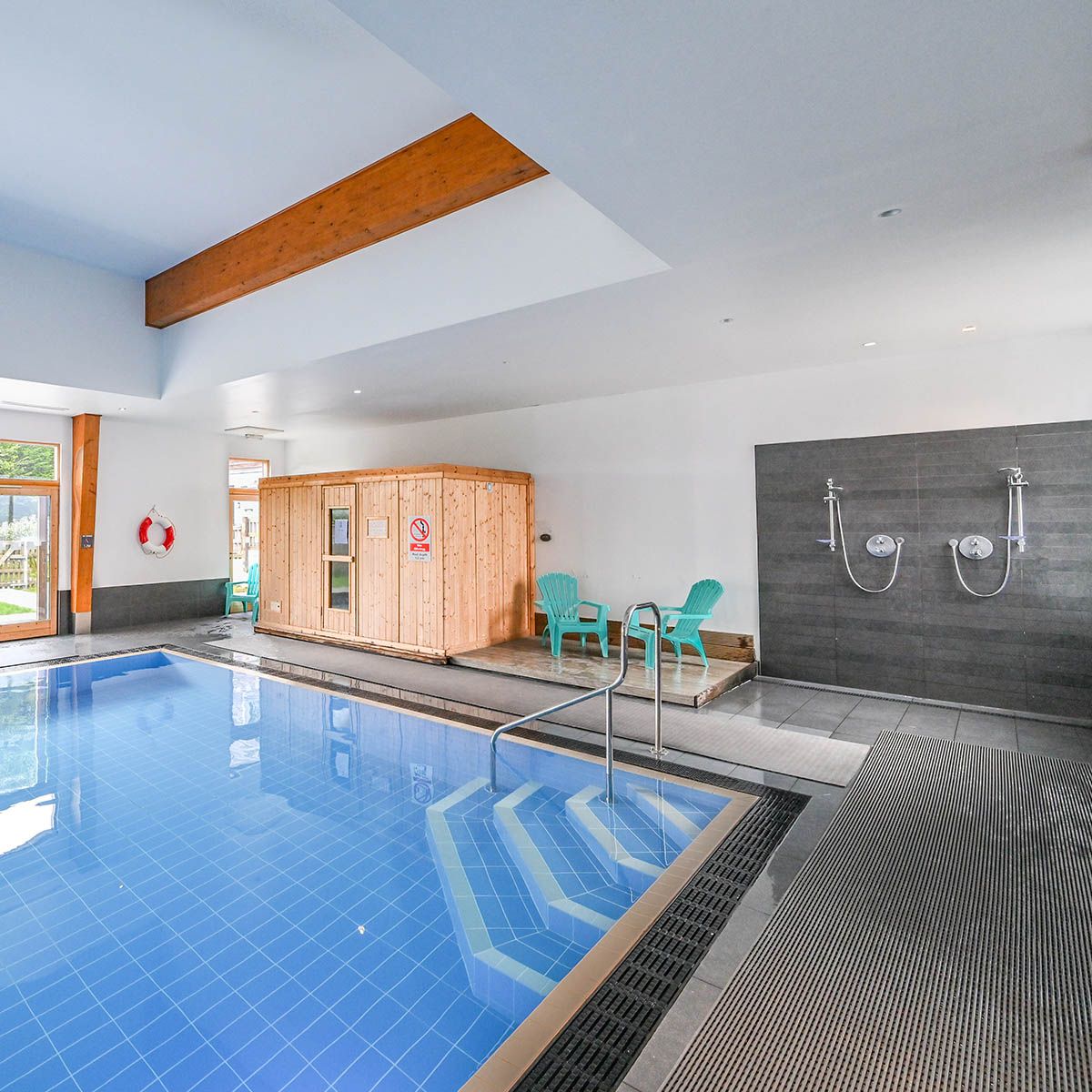 Indoor swimming pool with wooden sauna, showers, and seating area