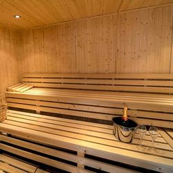 Interior of a wooden sauna with benches, a water bucket, and a champagne bottle with glasses.