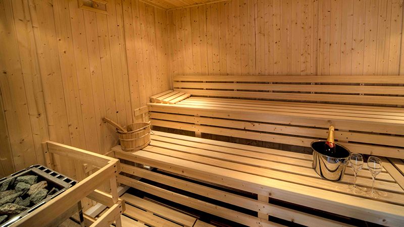 Interior of a wooden sauna with benches, a water bucket, and a champagne bottle with glasses.