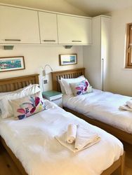 Two single beds in a bright bedroom with white bedding, wooden frames, colorful pillows, and artwork on the wall.