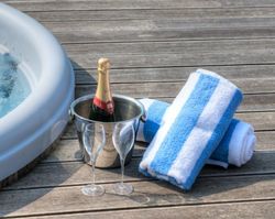 Champagne bottle in ice bucket with two glasses and striped towels next to a hot tub on wooden decking