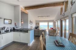 Open-plan kitchen, dining, and living area with large windows overlooking the sea