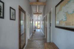 Bright hallway with stone floor, wooden beams, large mirror, framed map, and art on the walls.