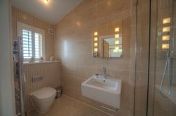 Modern bathroom with beige tiles, wall-mounted toilet, white sink, and glass shower enclosure