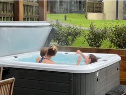 Two children relaxing in an outdoor hot tub with greenery in the background.