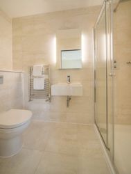 Modern bathroom with glass shower enclosure, wall-mounted sink, toilet, and heated towel rack.