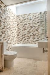 Modern bathroom with mosaic tile wall, bathtub, and toilet