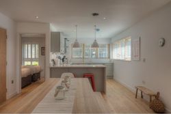 Modern kitchen and dining area with light wood flooring and white cabinetry. A bedroom is visible through an open doorway.