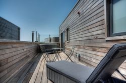 Modern wooden rooftop terrace with lounge chair, table, and two chairs under clear sky
